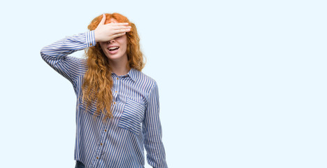 Wall Mural - Young redhead bussines woman smiling and laughing with hand on face covering eyes for surprise. Blind concept.