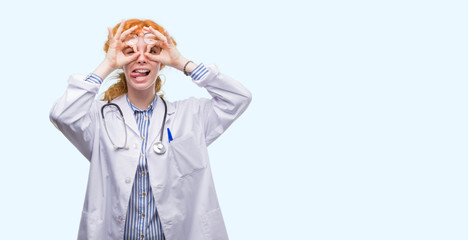 Poster - Young redhead woman wearing doctor uniform doing ok gesture like binoculars sticking tongue out, eyes looking through fingers. Crazy expression.