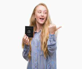 Canvas Print - Blonde teenager woman holding passport of Unites States of America pointing and showing with thumb up to the side with happy face smiling