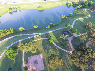 Wall Mural - Aerial urban lakeside green park in suburban area Houston. Trees, grassy lawn, playground, pathway, trail by lake shore for jogging, running, people exercising outdoor. Healthy lifestyle concept