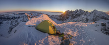 Yellow Tent Pitched Up On A Summit Of A High Alpine Peak. Winter Camping In Snow Covered Alpine Like Mountains. Winter Alpine Landscape, Climbing Bivouac Panorama. Vibrant Blue Sky, Sunset Or Sunrise.