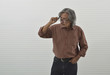 © grapestock - Suspicious asian senior businessman in red casual shirt and blue jeans taking off glasses and looking to something over white wall background