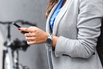 Wall Mural - Young businesswoman standing on street with bicycle looking at mobile phone.