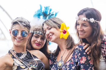 Wall Mural - four cheerful beautiful young women celebrate together and take a selfie picture smiling and having fun in friendship. party concept with colored dress and flowers crowd. bright background. 