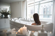 Pretty girl with wet hair having leisure in water with foam. She situating in wide beautiful apartment with flowers and candles. Lady washing during romantic atmosphere concept