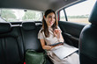 © Danon - A young attractive Japanese woman is reading an eBook on her tablet. She is doing this while on her way to work while riding a car which she booked via a ride hailing app.