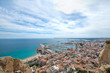 Wide angle view of Alicante, Spain from castle of Santa Barbara. Panoramic view of Postiguet beach, city and harbor. Mixed view of modern city and ruined fortress walls and towers.