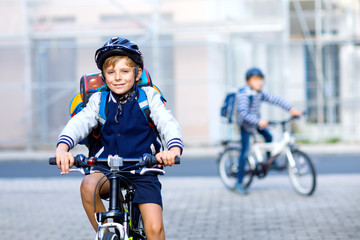 Two school kid boys in safety helmet riding with bike in the city with backpacks. Happy children in colorful clothes biking on bicycles on way to school. Safe way for kids outdoors to school