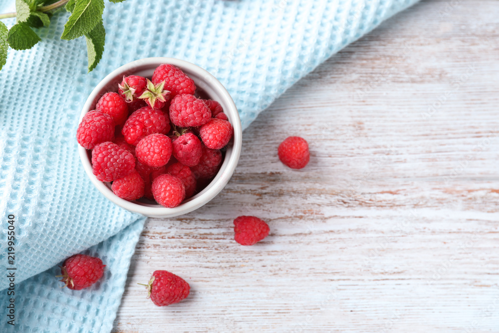 Bowl with ripe aromatic raspberries on wooden table