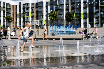 life of children in a modern city - little boy having fun with fountains