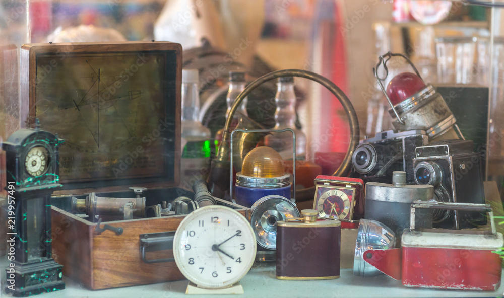 Assorted vintage items, clocks, cameras, flasks, sextant, lamps behind shop window. - obrazy, fototapety, plakaty 