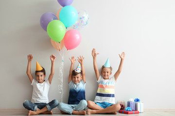 Poster - Cute little children in Birthday hats sitting on floor near light wall