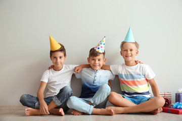 Cute little children in Birthday hats sitting on floor near light wall