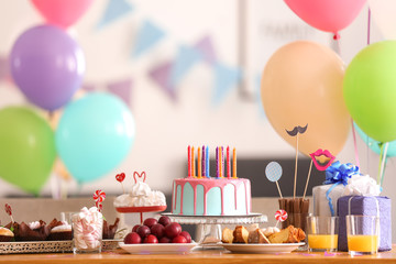 Beautiful birthday cake with candles and different sweets on table