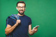 © denis_vermenko - Always in touch. Smiling young man holding smart phone and looking at it. Portrait of a happy man using mobile phone isolated over green background.