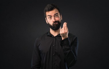 Handsome man with beard making money gesture on black background