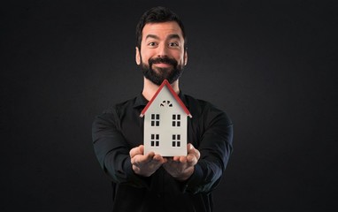 Handsome man with beard holding a little house on black background