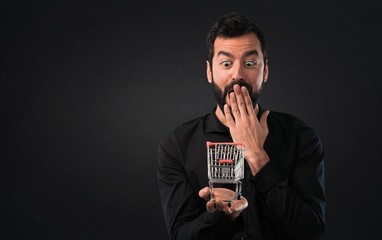 Wall Mural - Handsome man with beard holding a supermarket cart toy on black background