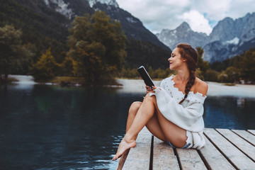 Wall Mural - Attractive young woman reading book on dock next to the lake