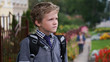 © cameravit - Little Caucasian curly boy in school uniform with backpack looking into the distance standing near school territory.