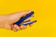hand holding a blue office stapler on a yellow background