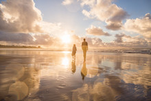 Father And Daughter Walking On An Ocean Beach During Sunset