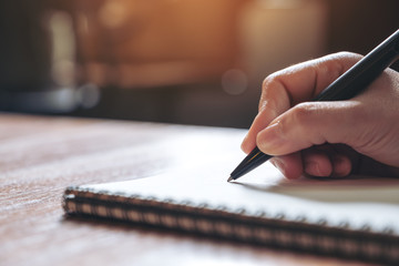 closeup image of a hand writing down on a white blank notebook on wooden table