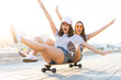 © opolja - Two smiling young girls having fun while riding on a skateboard at the park.