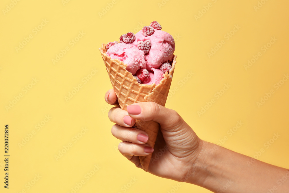 Woman holding waffle cone with delicious raspberry ice cream on color background