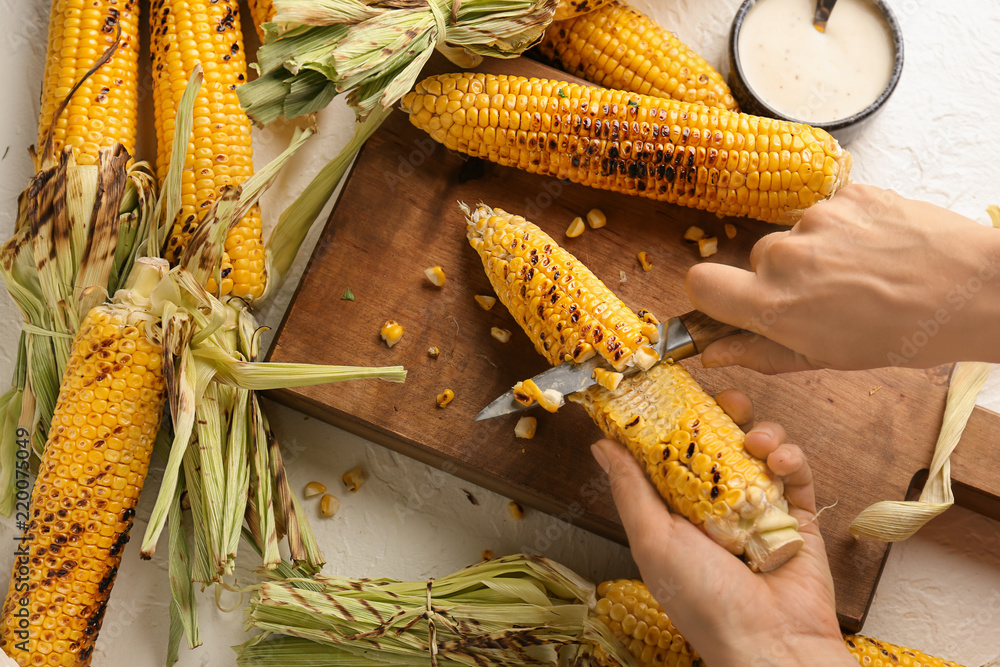 Woman cutting grilled corn cob on wooden board