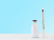 Blank label medical glass vial and plastic syringe for injection on white table with blue gradient background. Concept of vaccination, diabetes and cosmetic injection. Copy space.
