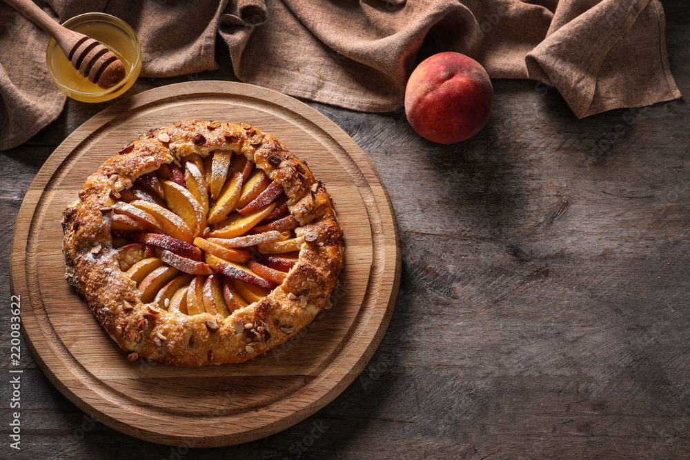 Board with delicious peach galette and honey on wooden table
