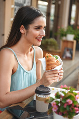 Woman sitting in cafe outdoors while eating croissant.