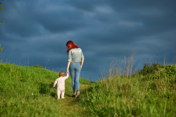 Wall Mural - Backview of young mother walking with little daughter in summer field.