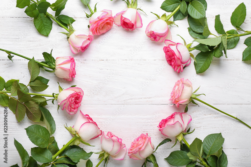 Frame made of beautiful roses on white wooden table