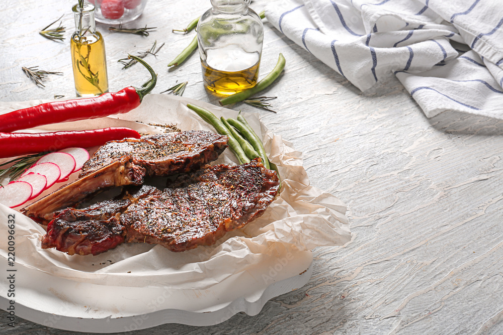 Parchment with delicious grilled steaks and vegetables on light wooden table