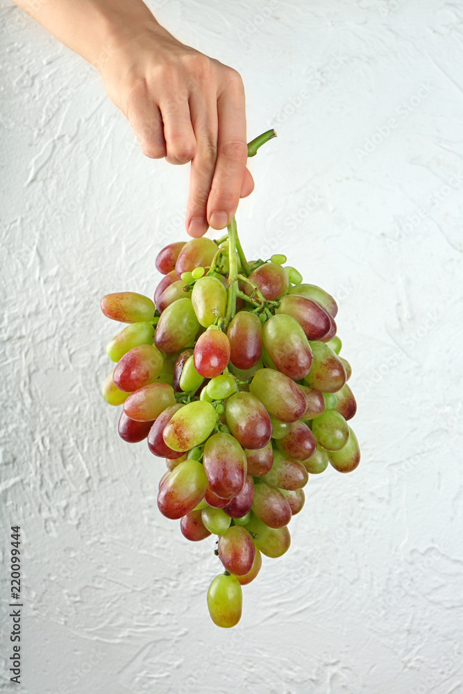 Woman holding fresh ripe grapes on white textured background