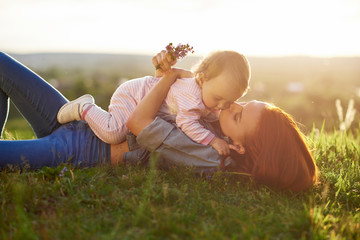 Wall Mural - Young mother kissing little daughter lying on grass.