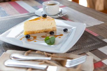 Wall Mural - cheesecake with blueberry sauce on white plate and cup of coffee on wooden table