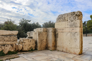 Chunks of marble forming a wall near the Athens Parthenon with trees and a blue cloudy sky behind