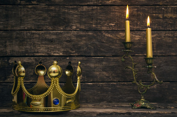 Wall Mural - Burning candle and king golden crown on aged wooden table background.