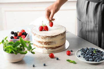 Woman decorating delicious cake with fresh berries at table. Homemade pastry