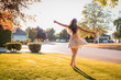 a woman in a dress twirling on a suburban front lawn in the summer at golden hour