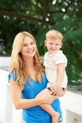 Cheerful little boy and his pretty young mother standing in park