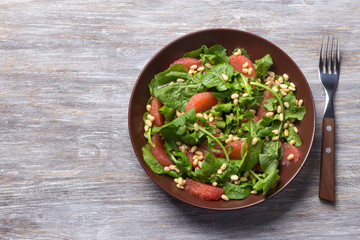 Fresh salad from arugula with grapefruit and pine nuts on a wooden background. Healthy delicious food