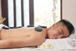© DragonImages - Smiling young Asian man relaxing with hot massage stones on his back