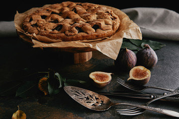 Wall Mural - close up view of homemade pie on baking paper, antique cutlery and fresh figs on dark tabletop