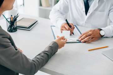 Wall Mural - cropped image of patient giving id card to doctor to fill insurance claim form in clinic