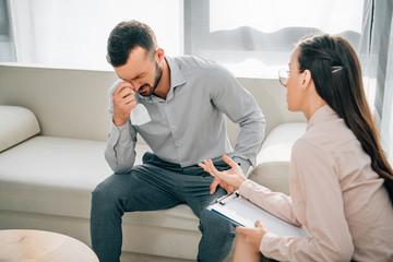 Wall Mural - psychologist with clipboard talking to crying male patient in office