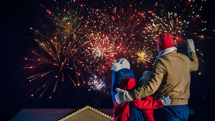 Wall Mural - Happy New Year Celebration, Young Family of Three Standing in the Front Yard Watching Beautiful Fireworks. In the Evening while Snow is Falling Father, Mother and Cute Little Daughter Look up.